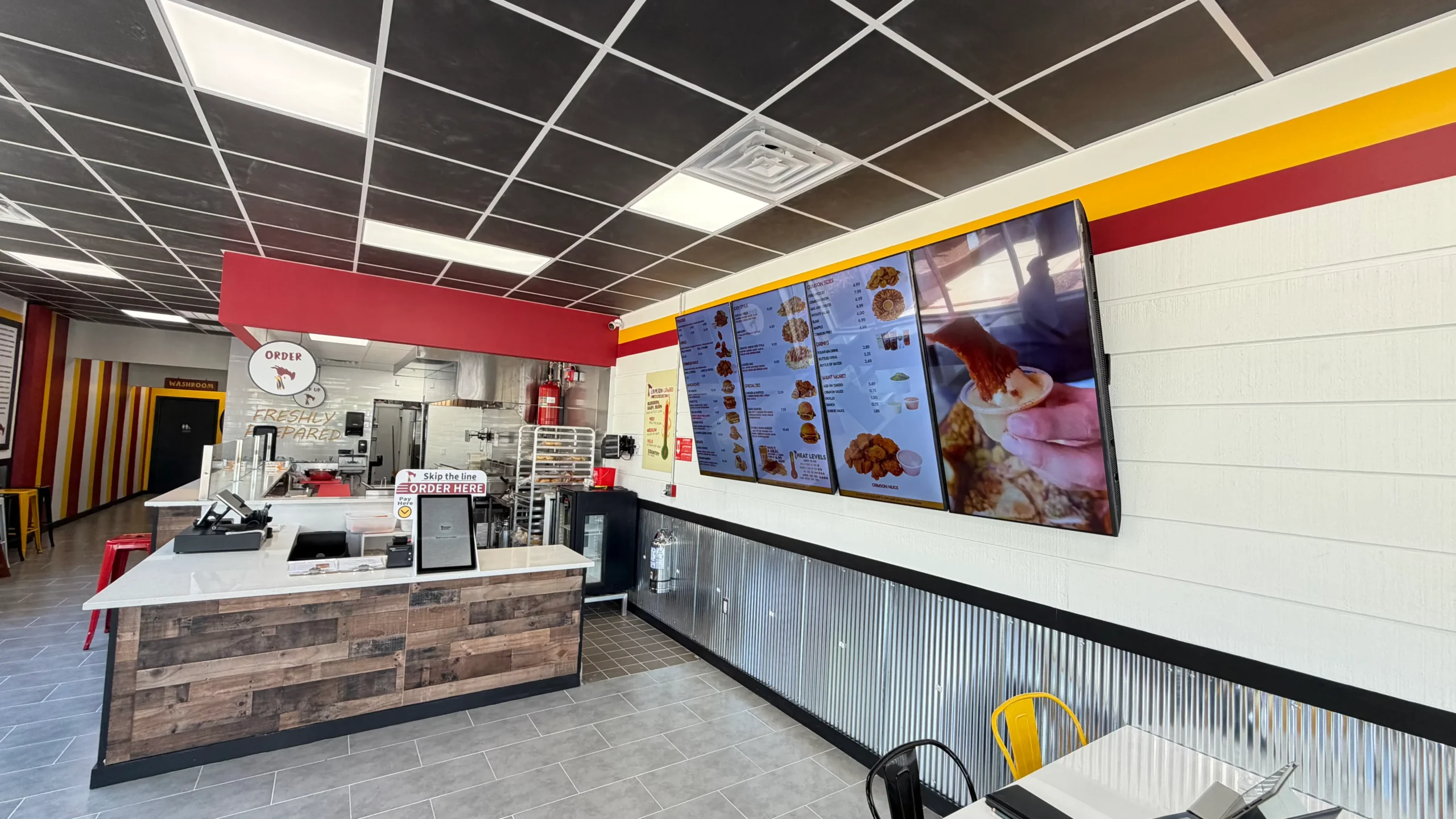Inside a Crimson Coward halal hot chicken franchise, showing the order counter, digital menu boards and dining area